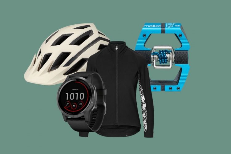 A collection of cycling gear including a white helmet, a black long-sleeve jacket, a black smartwatch displaying data, and a blue bike pedal. The background is a solid green color.