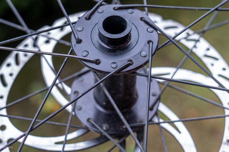 Close-up view of a bicycle wheel hub, showing the black hub with spokes attached to a disc brake rotor. The background is blurred, emphasizing the hub and spokes.
