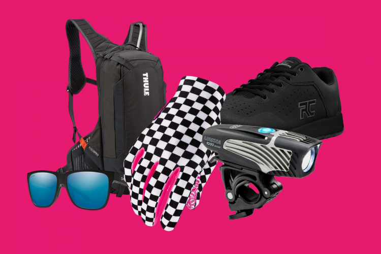 A black Thule backpack, checkered pink and black gloves, a pair of blue-tinted sunglasses, a black sneaker, and a bike light on a bright pink background.