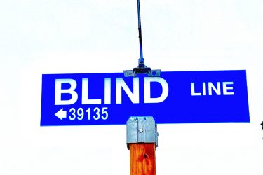 A blue street sign that reads "BLIND LINE," mounted on a wooden post, with the number "39135" below it. The background is a clear sky. Blind Line mountain bike trail.