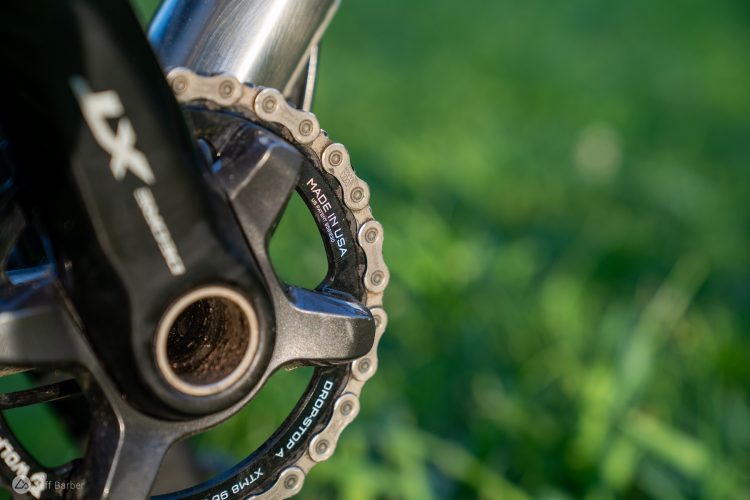 Close-up image of a bicycle crankset and chainring, showcasing the intricate design and gear details, set against a blurred green grass background.