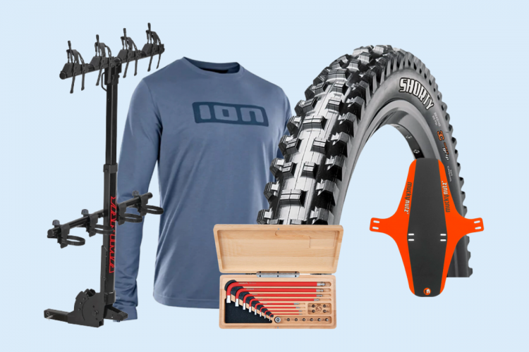 Image featuring various mountain biking gear, including a bike rack, a blue long-sleeve shirt, a mountain bike tire, a bike fender, and a set of tools in a wooden box, all arranged against a light blue background.