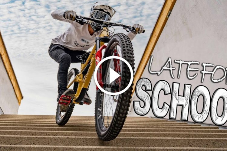 A person wearing a helmet and casual clothing rides a mountain bike down a set of stairs, showcasing an action-packed moment. The background features a cloudy sky, and the text "LATE FOR SCHOOL" is prominently displayed next to the cyclist.