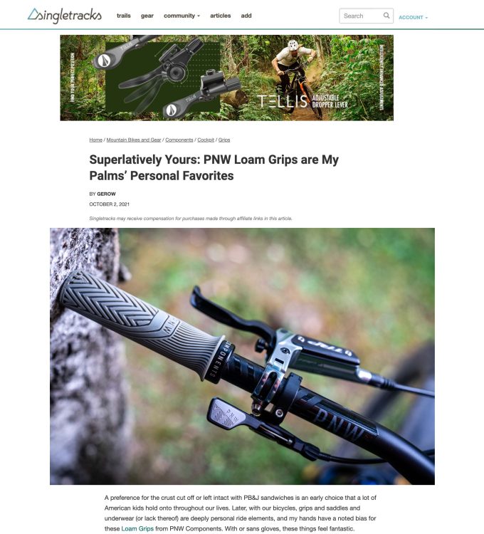 Close-up image of PNW Loam Grips mounted on a bicycle handlebar, featuring textured rubber grips and an adjustable dropper lever. The background shows a blurred natural setting, enhancing the focus on the grip design.