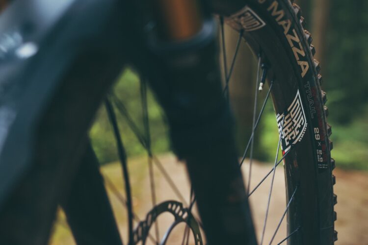 Close-up of a mountain bike tire and wheel, showcasing the treads and spokes against a blurred natural background. The tire is labeled with "Mazza" and "Trail" branding, emphasizing its suitability for off-road cycling.