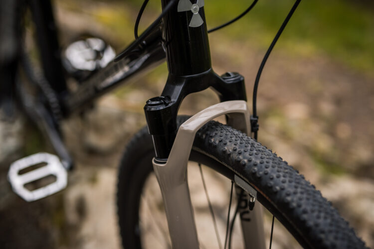 Close-up image of a bike's front suspension fork and tire, showcasing the textured surface of the tire and the sleek design of the fork against a natural background.