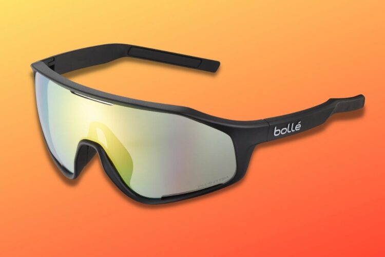 Black sports sunglasses with reflective lenses, featuring a curved design and a logo on the side, set against an orange gradient background.