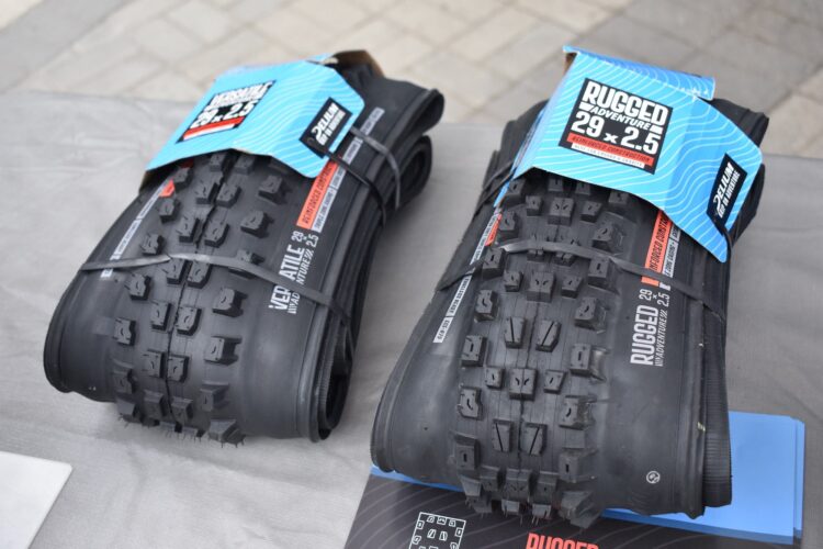 Two mountain bike tires are displayed side by side on a table. The tires are labeled "RUGGED 29 x 2.5" and are secured with straps. The tread pattern is prominently visible, indicating their off-road design.