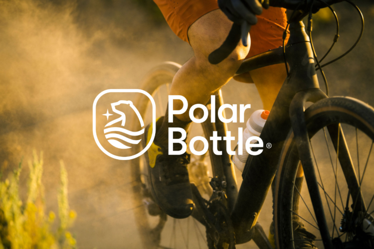 A close-up view of a cyclist riding on a dusty, outdoor trail, showcasing their leg in motion and a water bottle attached to the bike. The image features the Polar Bottle logo prominently in white, symbolizing hydration and outdoor adventure.