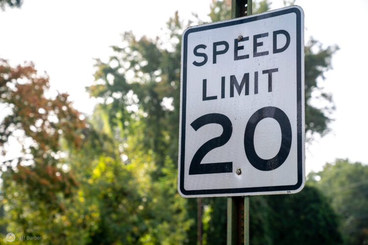 A clear speed limit sign indicating a limit of 20 miles per hour, mounted on a post, with blurred greenery in the background.