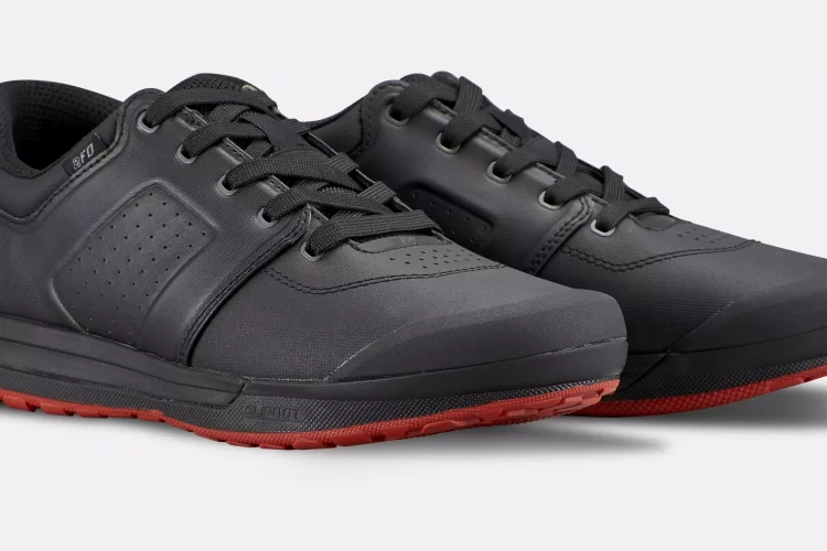A pair of black athletic shoes with a sleek design, featuring a smooth upper, round toe, and red rubber outsole. The shoes have a lace-up closure and perforated accents for breathability.