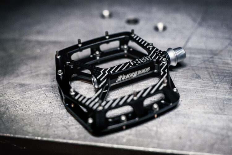 A black bicycle pedal with a textured surface and the brand name "Hope" visible, resting on a metallic surface. The pedal features several screw holes and has a sleek, modern design.