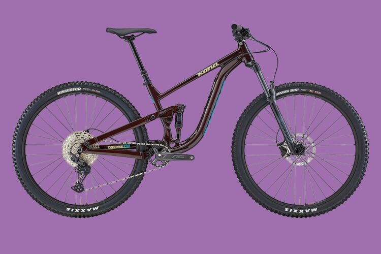 A mountain bike with a dark brown frame, featuring blue accents, and equipped with knobby tires. The bike has a modern design with a full suspension system, disc brakes, and a Shimano gear system, set against a vibrant purple background.