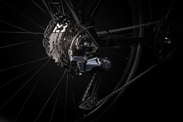 Close-up view of a bicycle's rear derailleur and cassette, highlighting the intricate details of the drivetrain components against a dark background.
