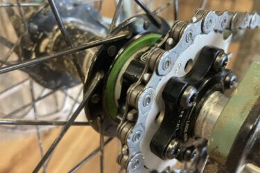 Close-up view of a bicycle hub and chain, showing the sprocket, chain, and surrounding components. The image highlights the intricate details of the hub, including dirt and wear, as well as the metallic chain links.