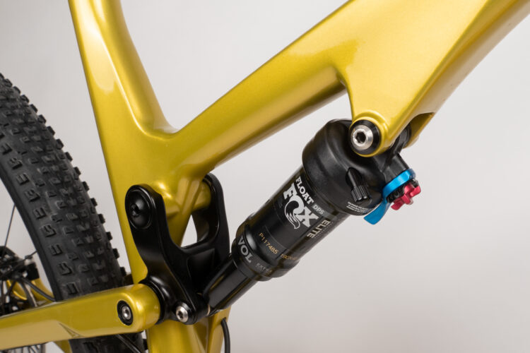 Close-up view of a gold-colored bicycle frame featuring a black FOX Float DPS shock absorber, showcasing the intricate design and components of the rear suspension system.