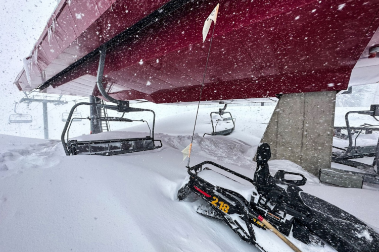 A snow-covered ski lift and surrounding area during a heavy snowfall, with snowdrifts piled high against the lift's base and chairs. icicles hang from the lift structure, while visibility is reduced due to the swirling snow.
