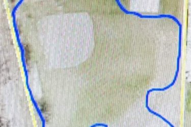 A map indicating property boundaries, featuring a blue outline that traces an irregular shape on a light background, with a few structures and roads visible within the area. Campus Life Single Track mountain bike trail.