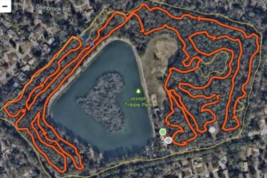 Map image showing the trail layout at Joseph Tribble Park, featuring a winding orange trail with directional arrows surrounding a central pond. The map includes nearby roads and residential areas. Tribble mountain bike trail.