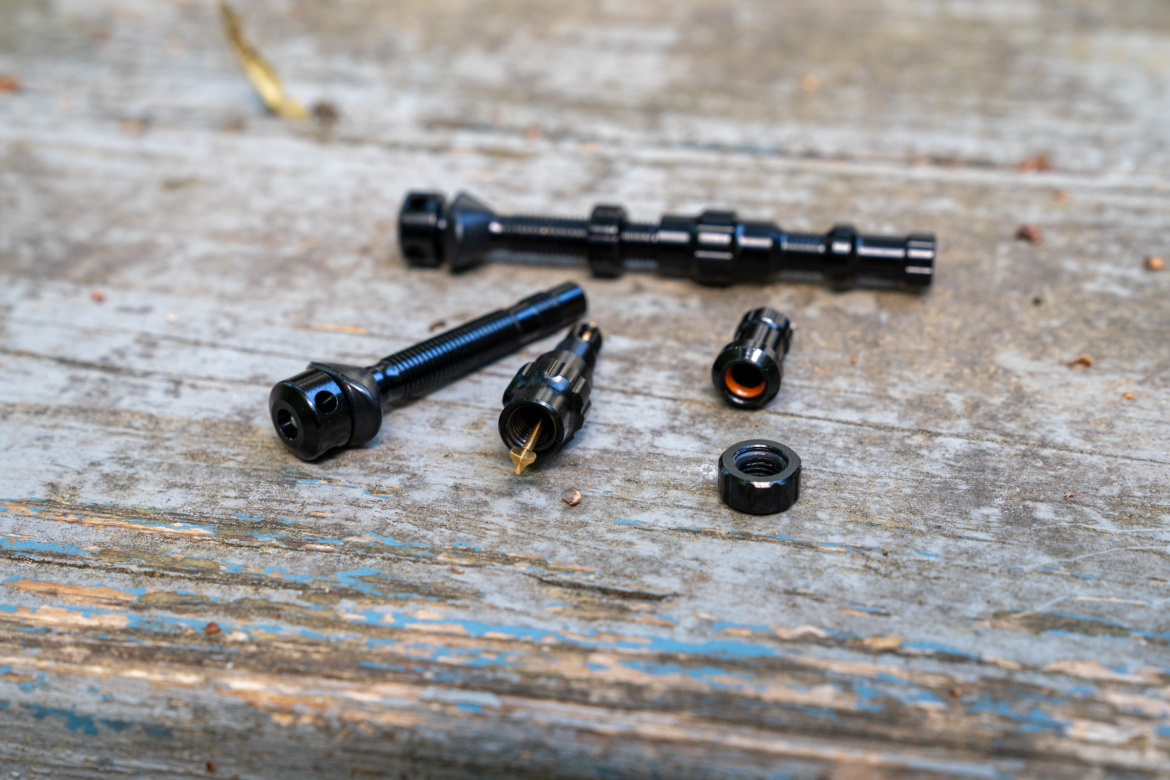 A collection of black fasteners, including screws, nuts, and connectors, arranged on a weathered wooden surface.