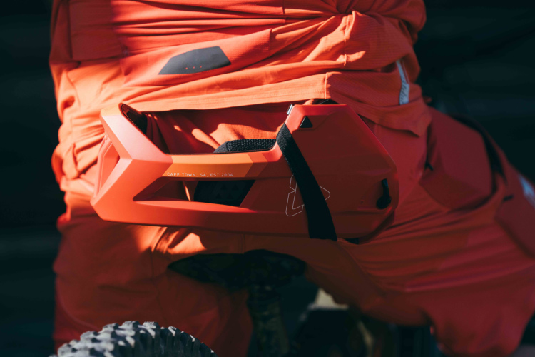 Close-up of a bright orange protective gear piece attached to the waist of a person wearing matching orange clothing, showcasing a modern design and branding details.