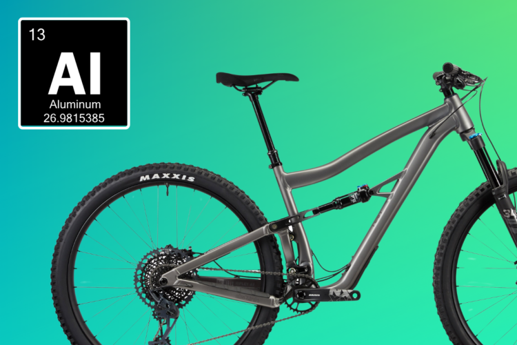 A close-up view of a modern mountain bike made from aluminum, featuring a sleek gray frame, Maxxis tires, and a detailed drivetrain. To the left, there is an illustration displaying the chemical element symbol "AI" for Aluminum, along with its atomic number (13) and atomic weight (26.9815385), all set against a gradient green background.