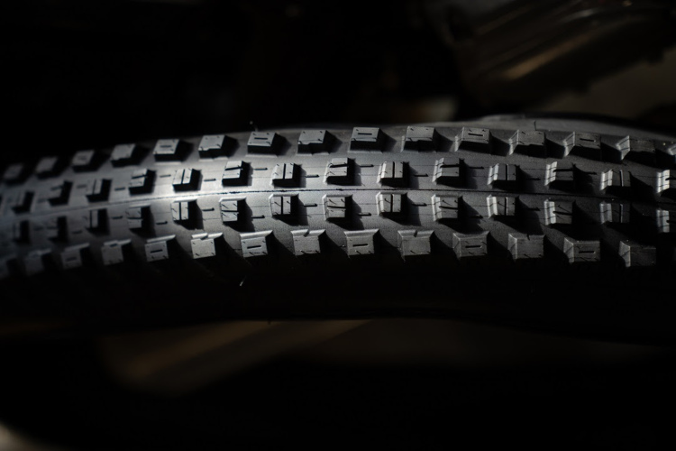 Close-up view of a textured black tire tread, featuring distinct patterns and grooves, set against a dark background.