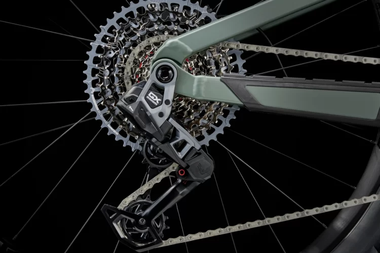 Close-up view of a bicycle's rear drivetrain components, featuring a green bike frame, a cassette with multiple gears, and a derailleur showcasing intricate mechanics against a dark background.