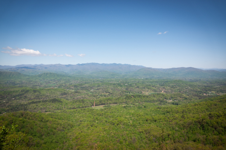 A panoramic view of lush green valleys and rolling mountains under a clear blue sky, showcasing the vibrant natural landscape in spring.