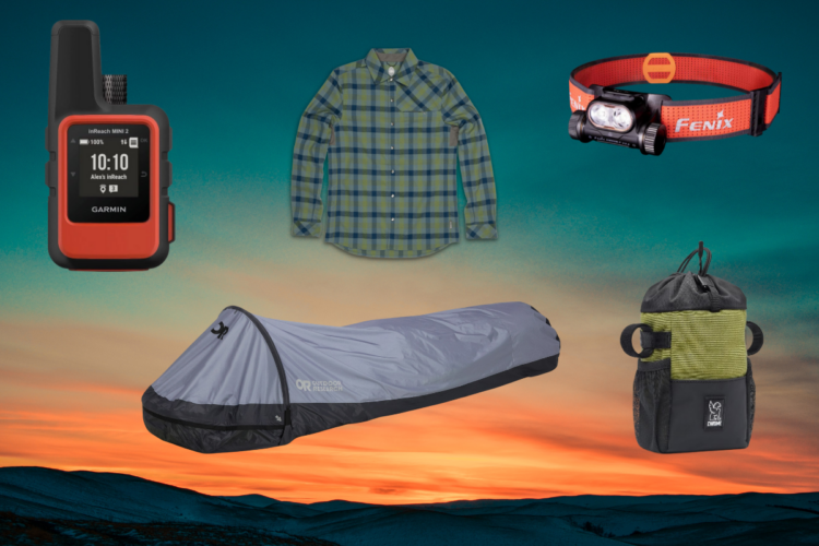 A collection of outdoor gear displayed against a scenic background featuring a sunset. Items include a red Garmin inReach Mini 2 satellite communicator, a green and blue plaid long-sleeve shirt, a gray sleeping bag, a Fenix headlamp, and a small black and green storage bag.