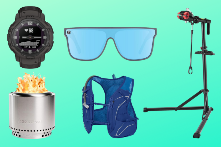 A flat lay image featuring a black Garmin solar watch displaying heart rate, a pair of blue sunglasses, a silver portable camping stove with flames, a blue hydration backpack, and a bicycle repair stand against a gradient green background.