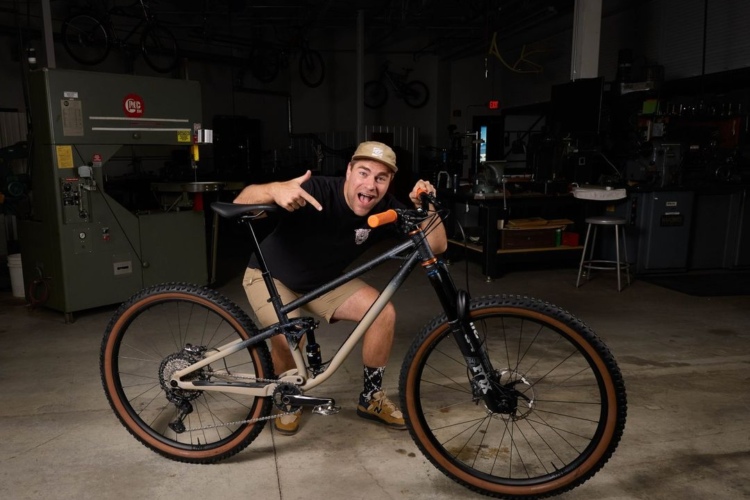 Kyle Neuser poses with his design, the steel Trek Pipe Dream full suspension mountain bike in a workshop setting.