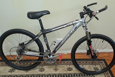 Trek 4300: A silver Trek mountain bike with thick black tires, a comfortable seat, and a front suspension fork. The bike is positioned on a patterned rug in a room with a light-colored wall.