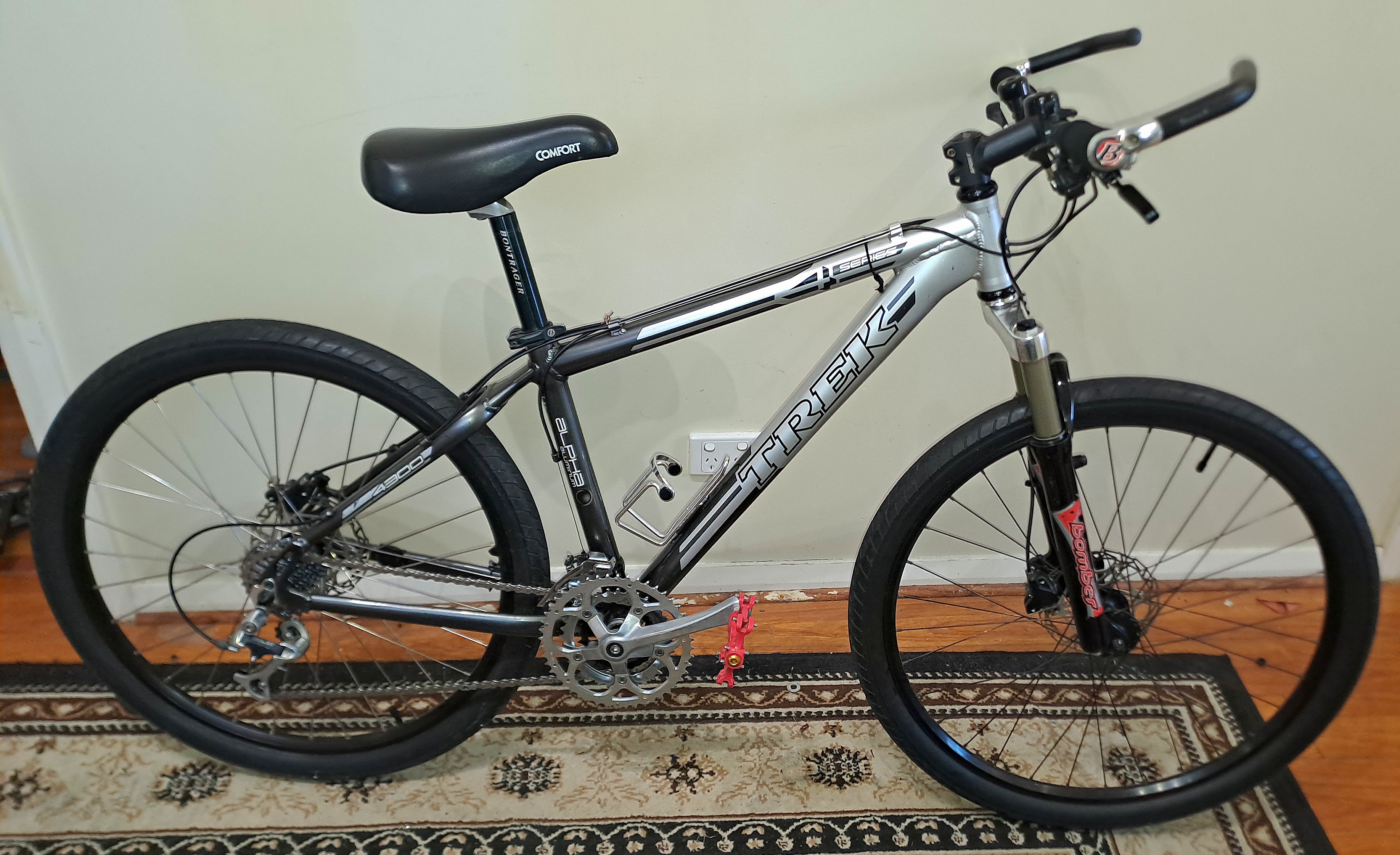 Trek 4300: A silver Trek mountain bike with a comfortable seat, disc brakes, and a black frame stands on a patterned rug against a light-colored wall.