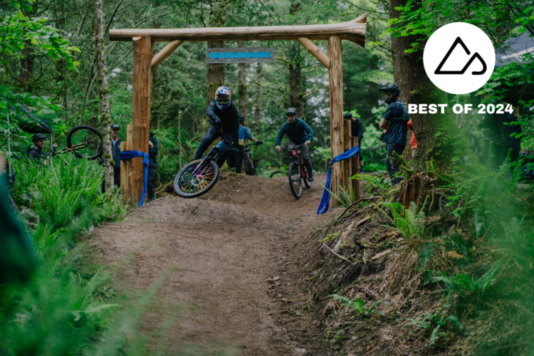 A mountain biker performs a stunt on a dirt track, riding past a wooden archway in a forested area. Surrounding the track, spectators watch as lush greenery lines the path. A "Best of 2024" logo is displayed in the corner of the image.