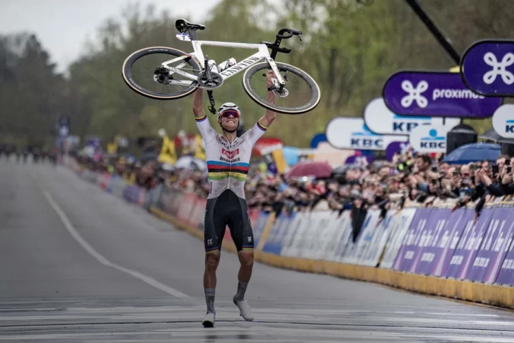 Mathieu van der Poel celebrates victory by raising their bike above their head at the finish line, surrounded by an enthusiastic crowd with banners and flags.