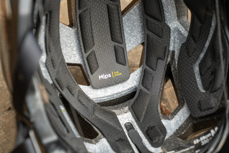 Close-up view of the interior of a bicycle helmet, showcasing the Mips (Multi-directional Impact Protection System) technology and padding. The helmet features a combination of foam materials designed for safety and comfort, with a focus on ventilation and fit. The light grey and black elements are visible, along with branding details.