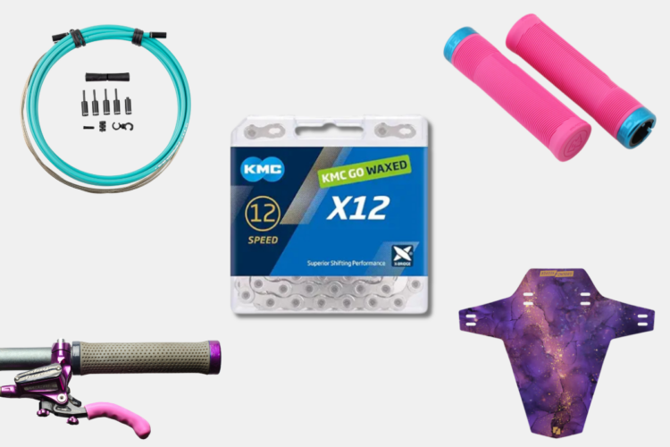 A collection of bicycle components including a turquoise cable and assorted fittings, a package of KMC 12-speed waxed chain, two pink bicycle grips with blue accents, and a purple and gold galaxy-themed bike fender.