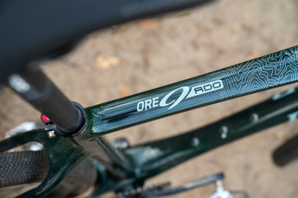 Close-up of a green bicycle frame featuring the text "ORE" and "9 RDO," showcasing a sleek design with a topographic pattern along the top tube.