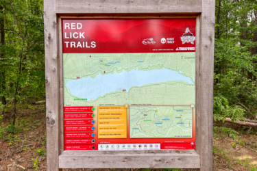 Information sign for Red Lick Trails featuring a detailed map of the area, listing various trails with their lengths and difficulty levels, surrounded by greenery. Red Lick Trails mountain bike trail.