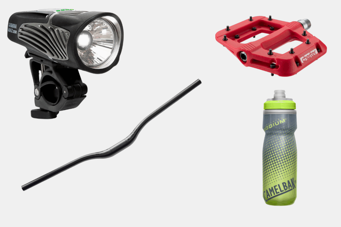 Image alt text: A collection of cycling accessories including a black bike headlight, a red bike pedal, a curved black handlebar, and a gray and green CamelBak water bottle.