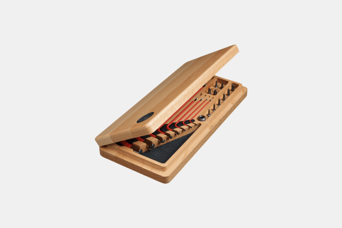 Alt text: A wooden tool kit box partially opened, revealing red-handled tools and various small fixtures inside. The box has a smooth finish and a logo on the top.
