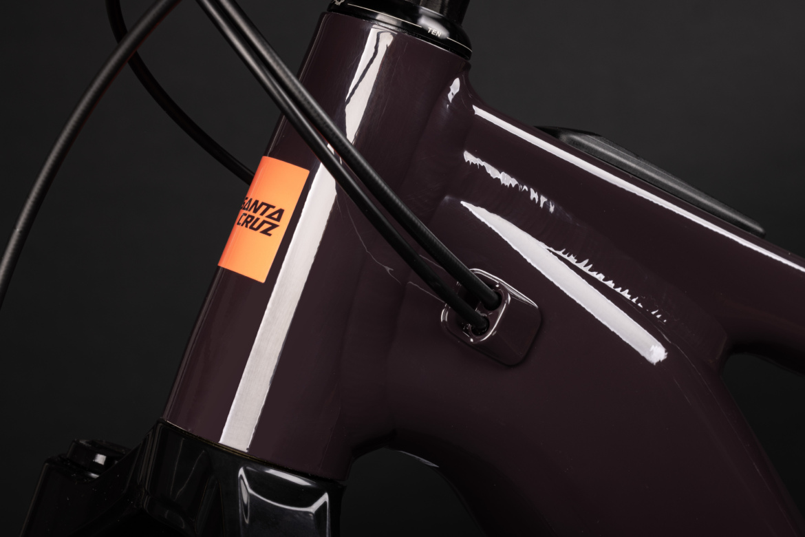 Close-up view of a purple bicycle frame featuring the brand label "Santa Cruz." The image highlights the frame's glossy finish, cable routing, and design details against a black background.