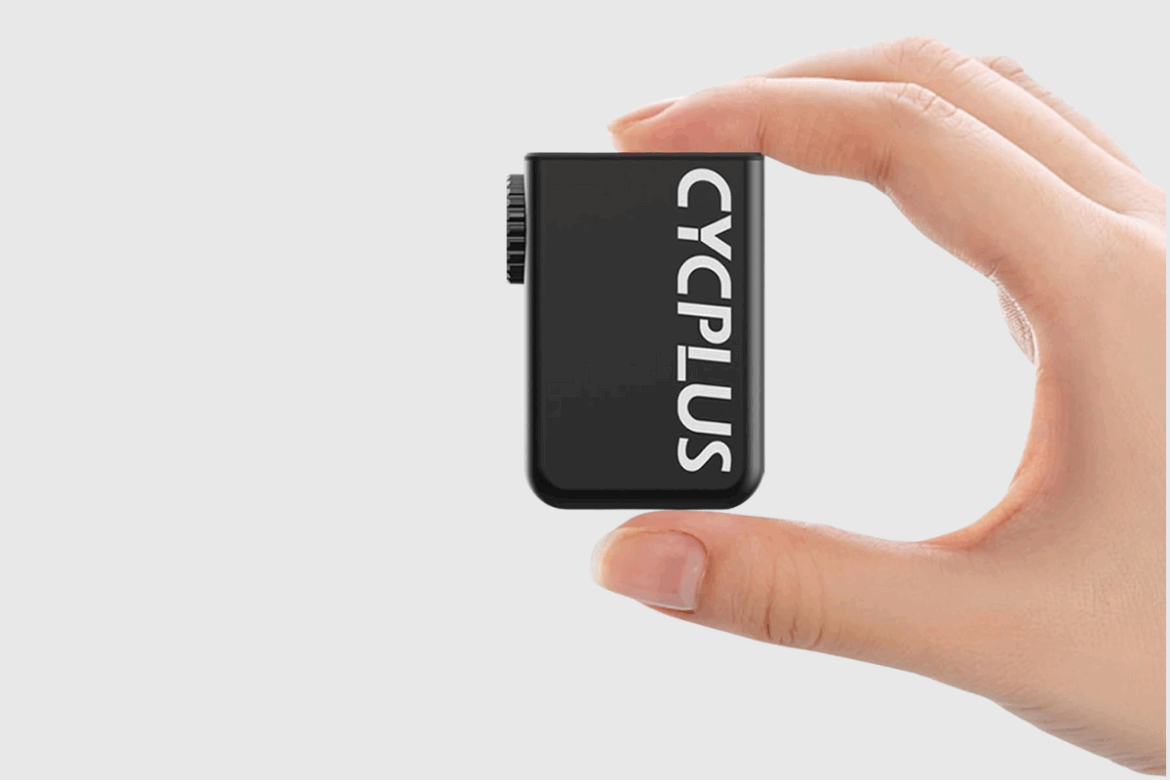 A person holding a small black device labeled "CYCPLUS," showcasing its compact size against a plain gray background.