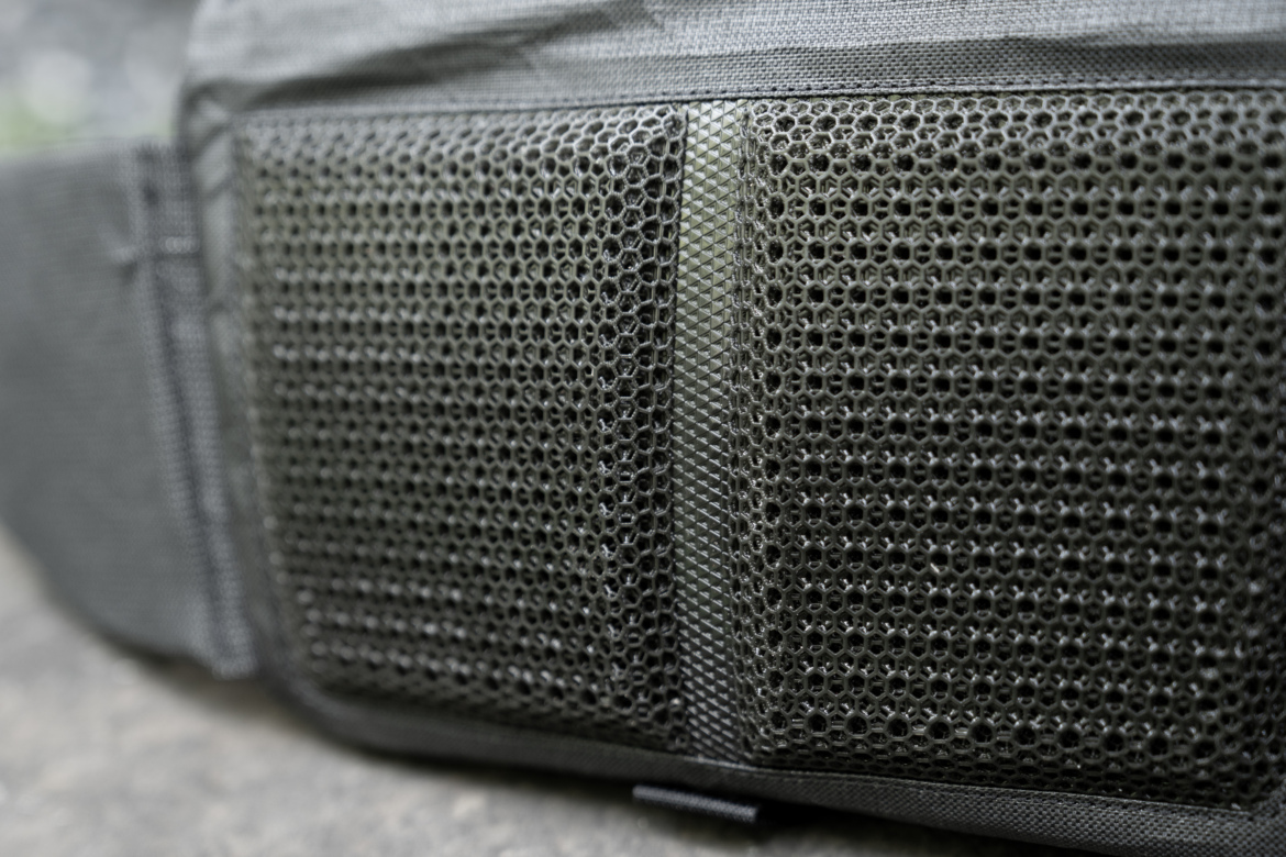 Close-up of a textured, black material featuring a honeycomb mesh pattern, typically used in bags for breathability and comfort.