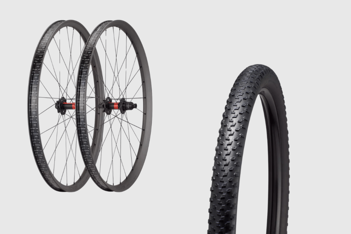 A close-up image of two bike wheels with black rims and spokes, showing a rear hub with a red accent. To the right, there is a mounted black tire with a textured tread pattern, suitable for off-road use. The background is plain, highlighting the bike components.