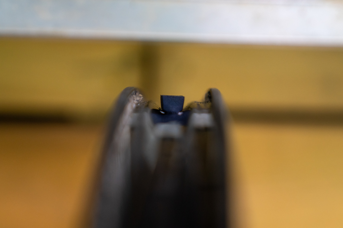 Close-up view of the edge of a mechanical component, showing a narrow gap with a small rectangular piece in the center. The background is blurred with muted colors.