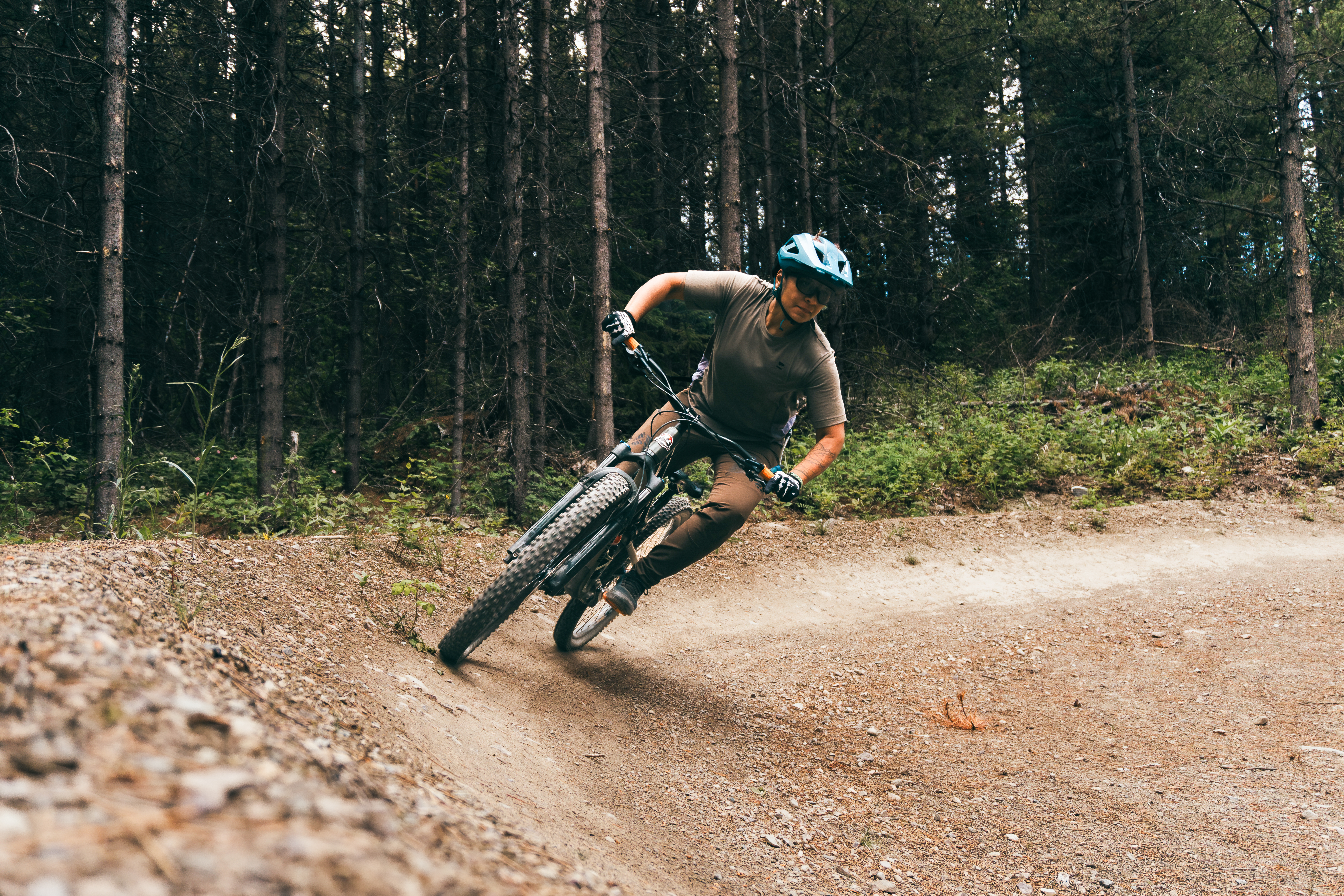 A mountain biker leaning into a turn on a dirt trail surrounded by tall trees. The rider is wearing a helmet and biking gear, with one foot raised off the ground as they navigate the curve of the path. Mount Harry Davis mountain bike trail.