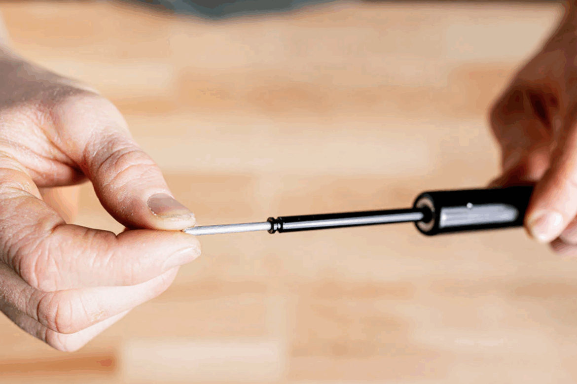 A person holding a screwdriver with a close-up view of the tip against a blurred wooden background.