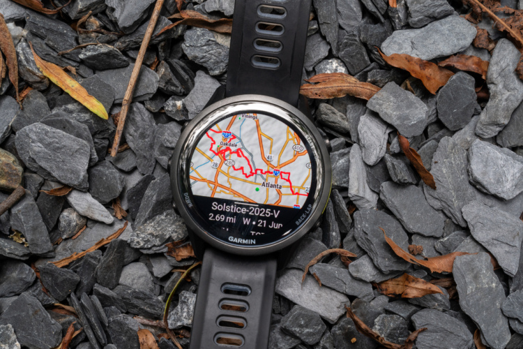 A close-up of a Garmin smartwatch displaying a detailed map of Atlanta on a rocky surface, surrounded by small pieces of gray stone and some dried leaves. The watch shows distance information and is positioned at an angle to highlight its features.